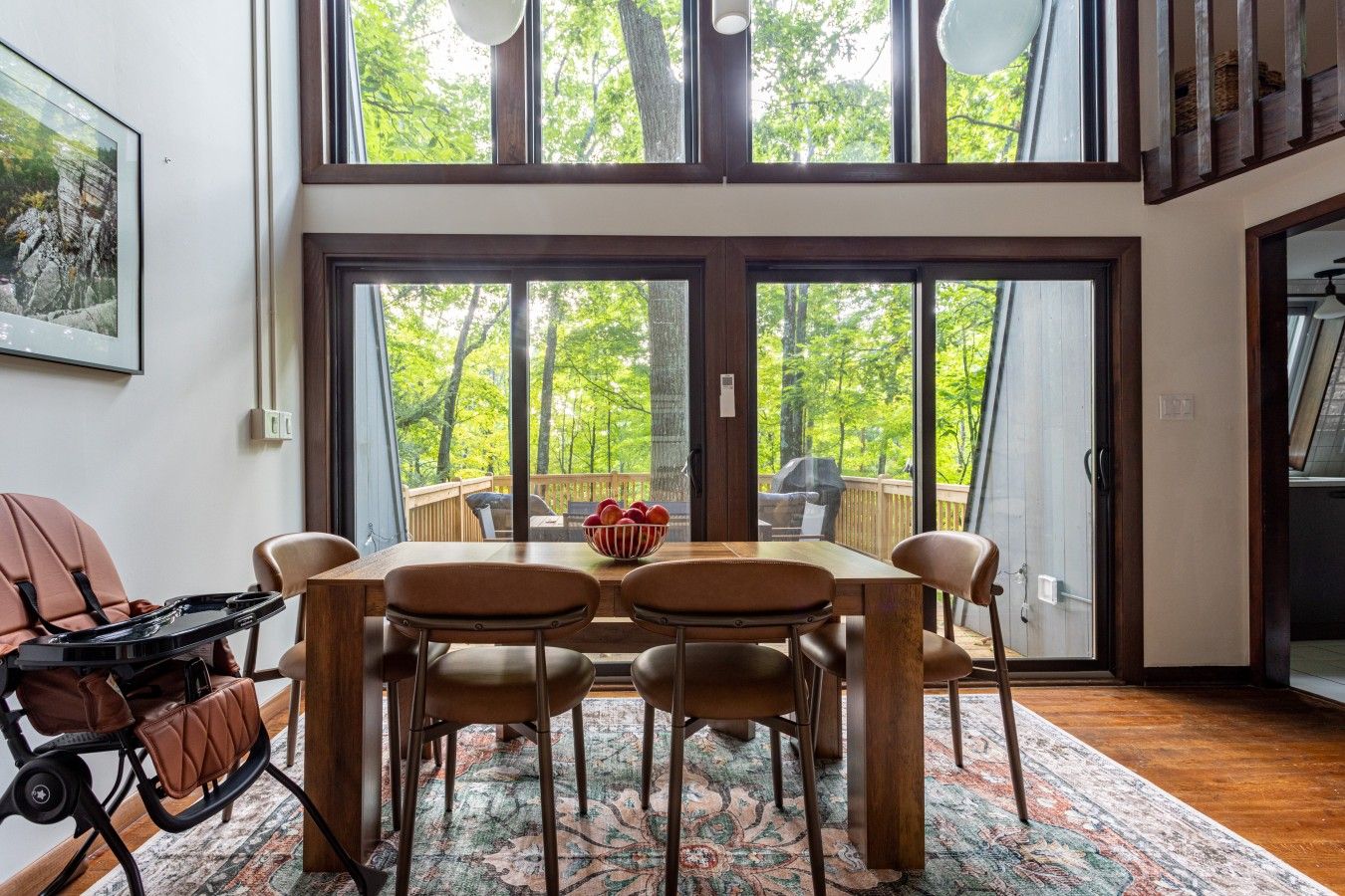 Un coin repas avec une table et des chaises, un saladier rempli de fruits, et une vue sur l’extérieur grâce à de grandes portes-fenêtres coulissantes.