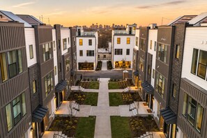 A modern apartment complex with a central courtyard, multiple balconies, and a city skyline in the background. - Game-day rooftop & fire pit retreat near Geodis Park, sleeps 12 (Nashville)