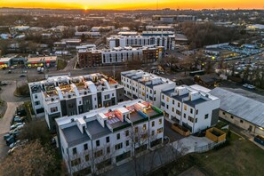 A multi-story building with a rooftop terrace, parking lot, and adjacent smaller structures. - Fall in Nashville: sleeps 12, 2-car garage & fire pit, near Broadway & Geodis (Nashville)