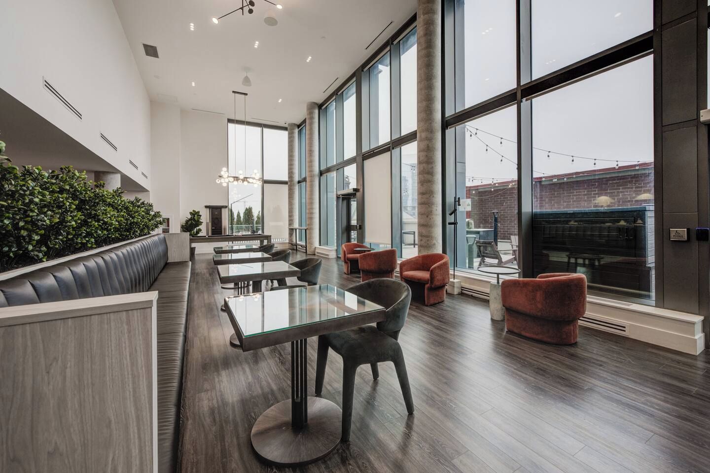 Un intérieur moderne avec une longue table à manger, de nombreuses chaises, un canapé et de grandes fenêtres donnant sur l’extérieur.