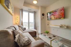 A modern living room with a sectional sofa, a glass coffee table, and a large painting on the wall. - Modern Condo in Central KW w/ Gym (Kitchener)
