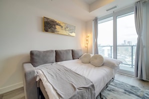A modern bedroom with a large bed, a city view, and a painting on the wall. - Modern Condo in Central KW w/ Gym (Kitchener)