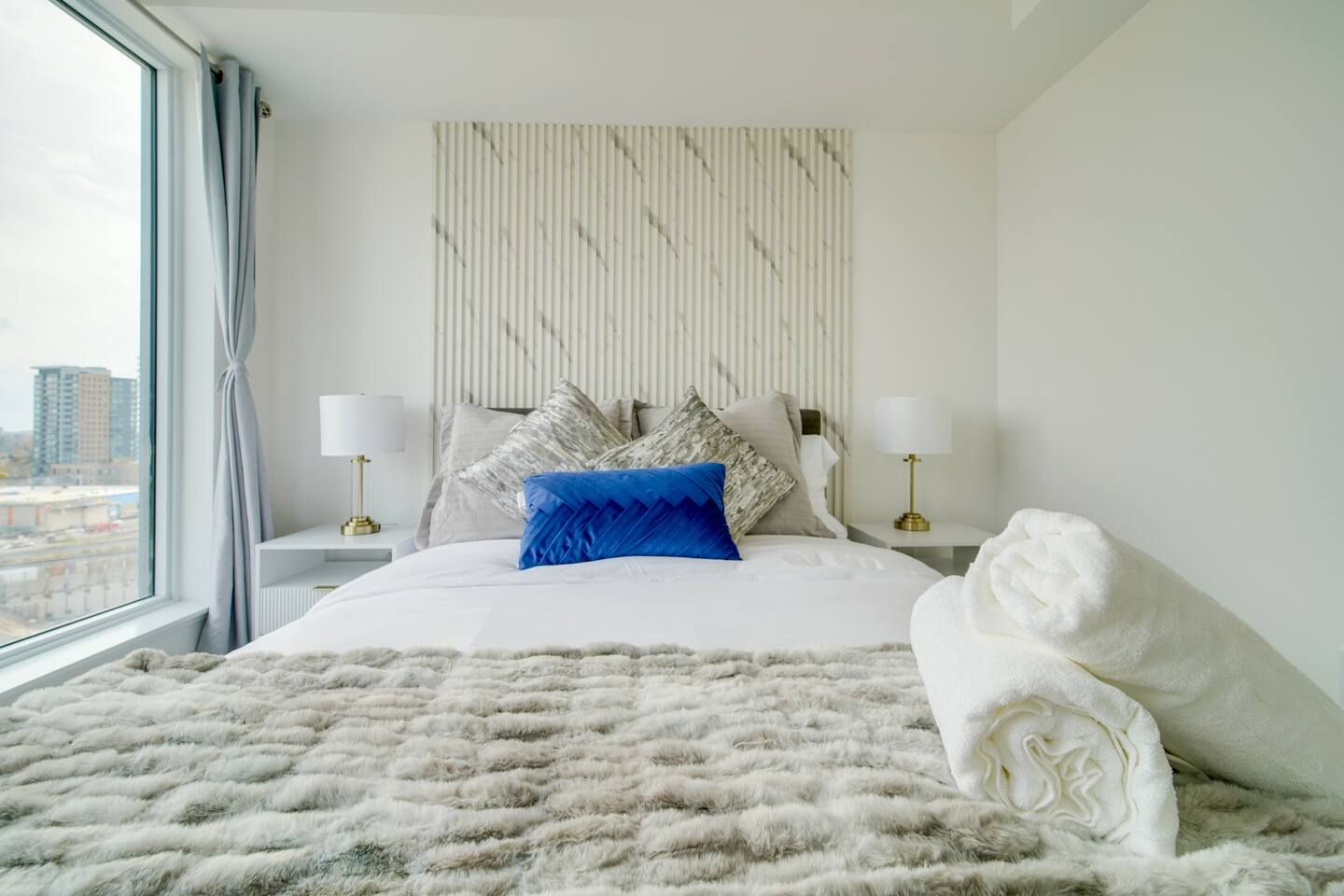 A hotel room with a large bed, two bedside tables, a window with curtains, and a city view.