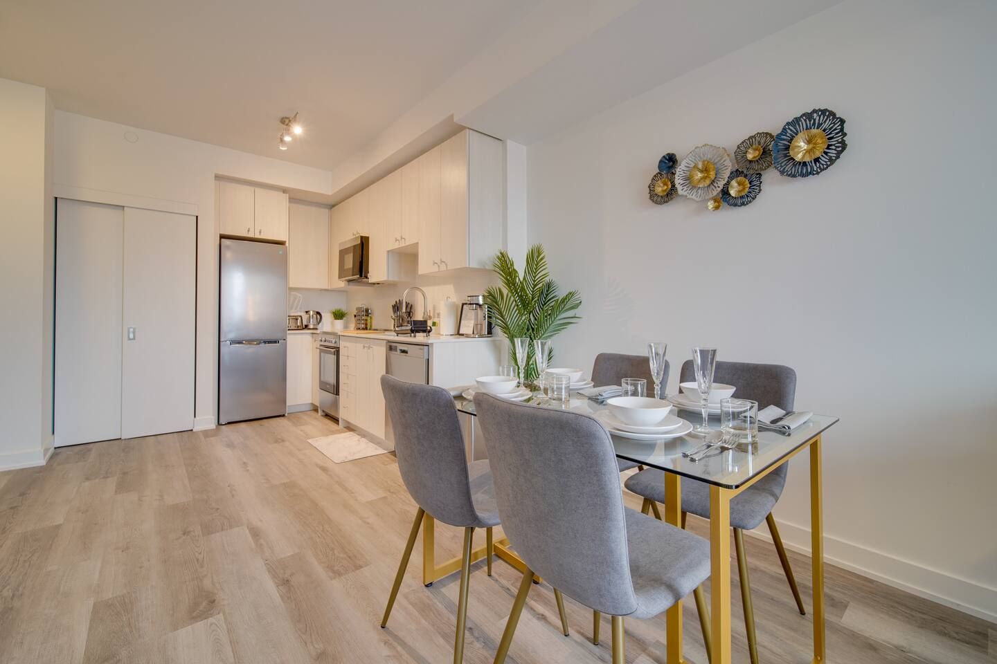 A modern kitchen with a dining area, featuring a table set for four, a refrigerator, and a sink.