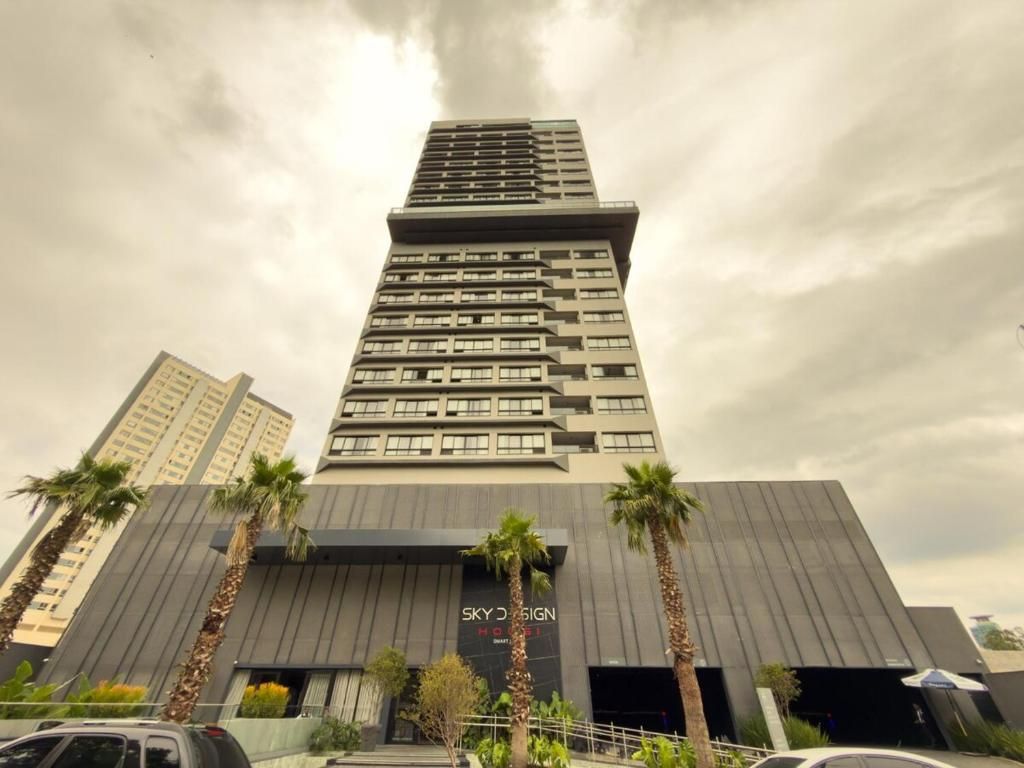 Un edificio de hotel alto con un diseño moderno, que presenta una entrada destacada y un letrero que dice 'SKY DESIGN HOTEL'.