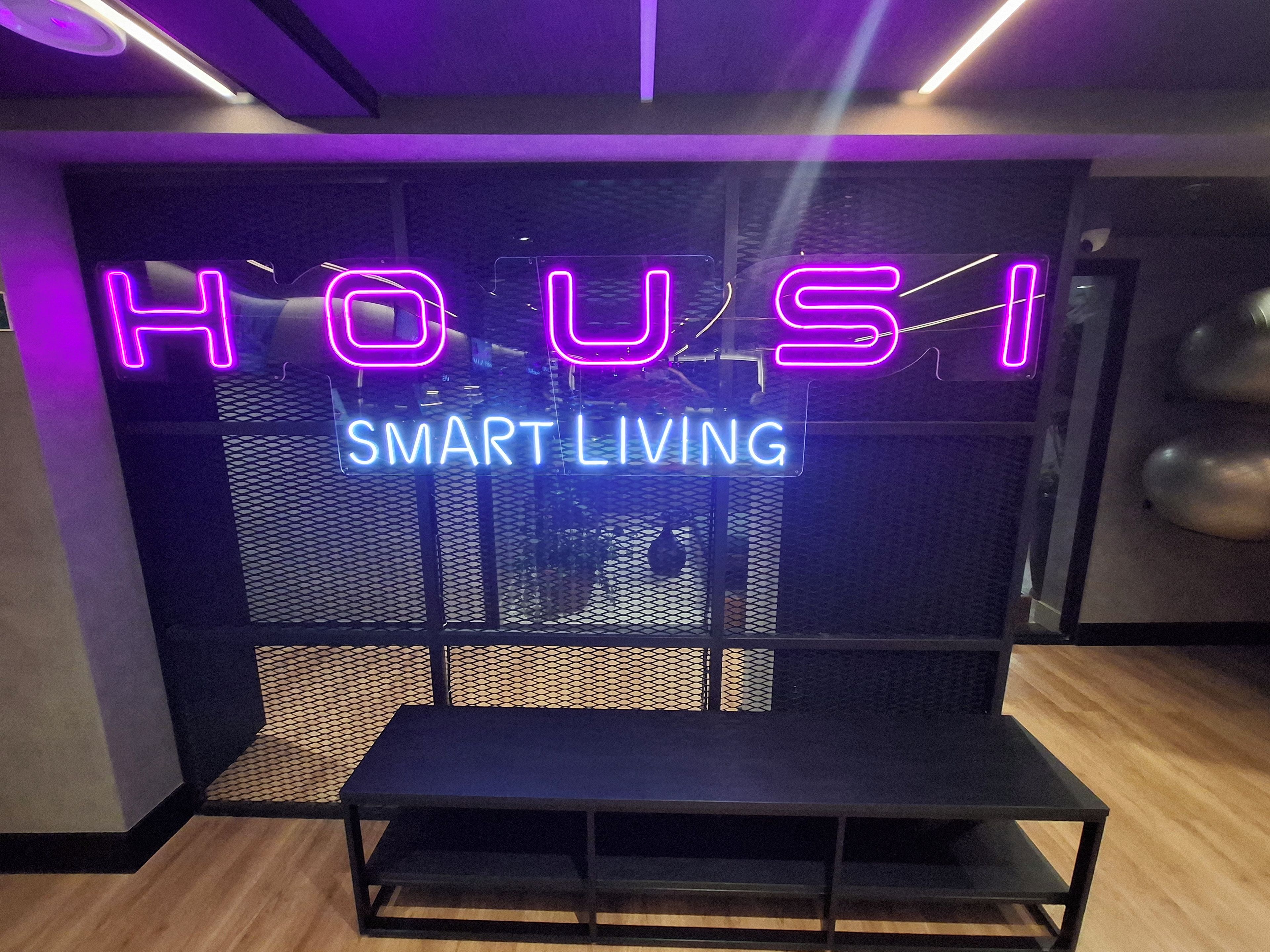 Una habitación con un letrero de neón que dice 'HOUSI SMART LIVING' y un banco negro al frente.