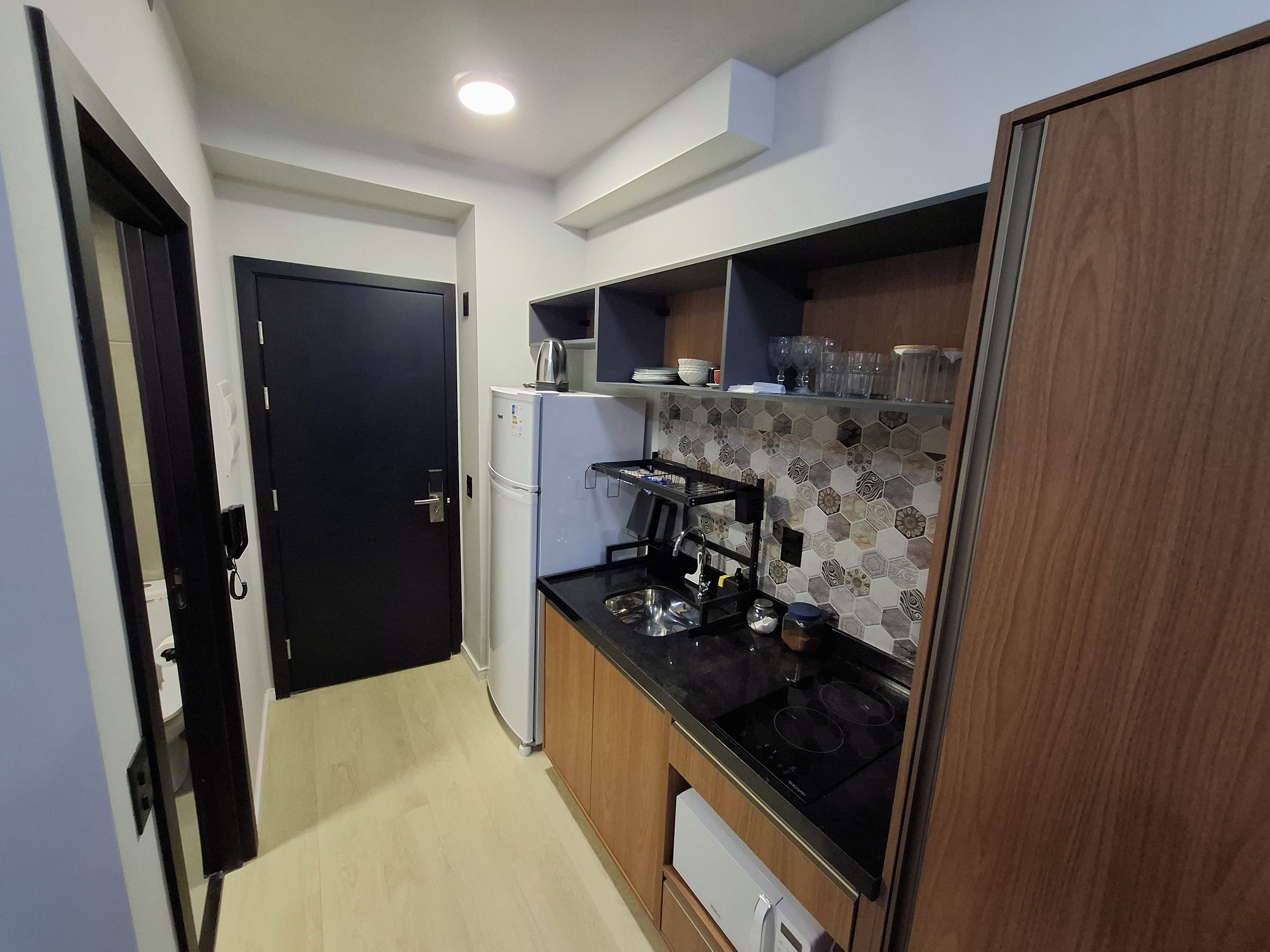 Cocina compacta con refrigerador, estufa y microondas. Hay una puerta que da a otra habitación.