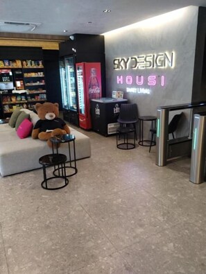 Een moderne lounge met een bank, een teddybeer en een neonbord met de tekst 'SKYDESIGN HOUSI'.