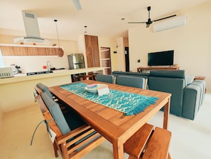 A modern kitchen with a built-in stove and refrigerator, a dining area with a wooden table and chairs, and a living room with a sofa and a flat-screen TV. - Jungle Retreat with 2 Pools & Cenotes in vibrant Tulum (Tulum)