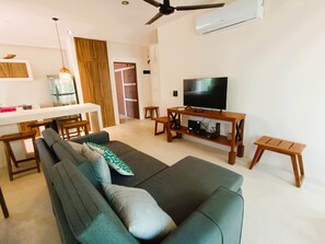 A modern living room with a sofa, TV, wooden side table, and a dining area with a table and chairs. - Jungle Retreat with 2 Pools & Cenotes in vibrant Tulum (Tulum)