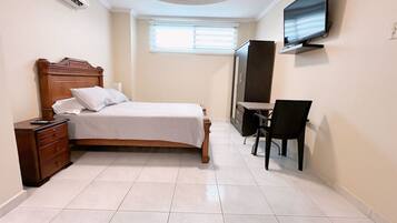 Un dormitorio con cama, cómoda, escritorio, silla, televisor y ventana.