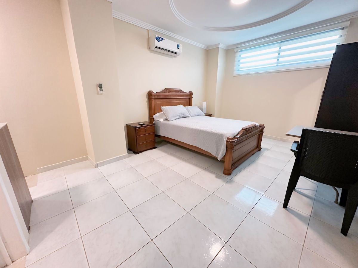 A bedroom with a bed, bedside table, dresser, and a window with blinds.