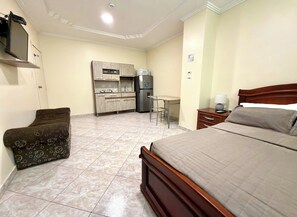 A hotel room with a bed, a desk, a chair, a kitchenette, and a TV.