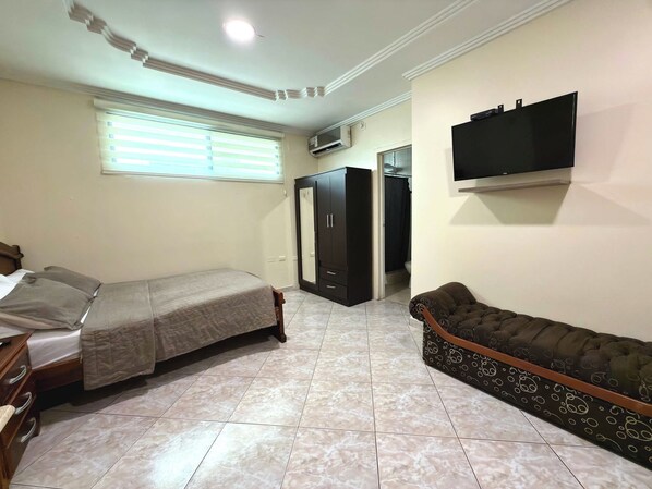 A bedroom with a bed, a sofa, a wardrobe, a television, and a window with blinds.