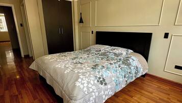Un dormitorio con una cama grande, suelo de madera, cabecera oscura y una lámpara en el techo.