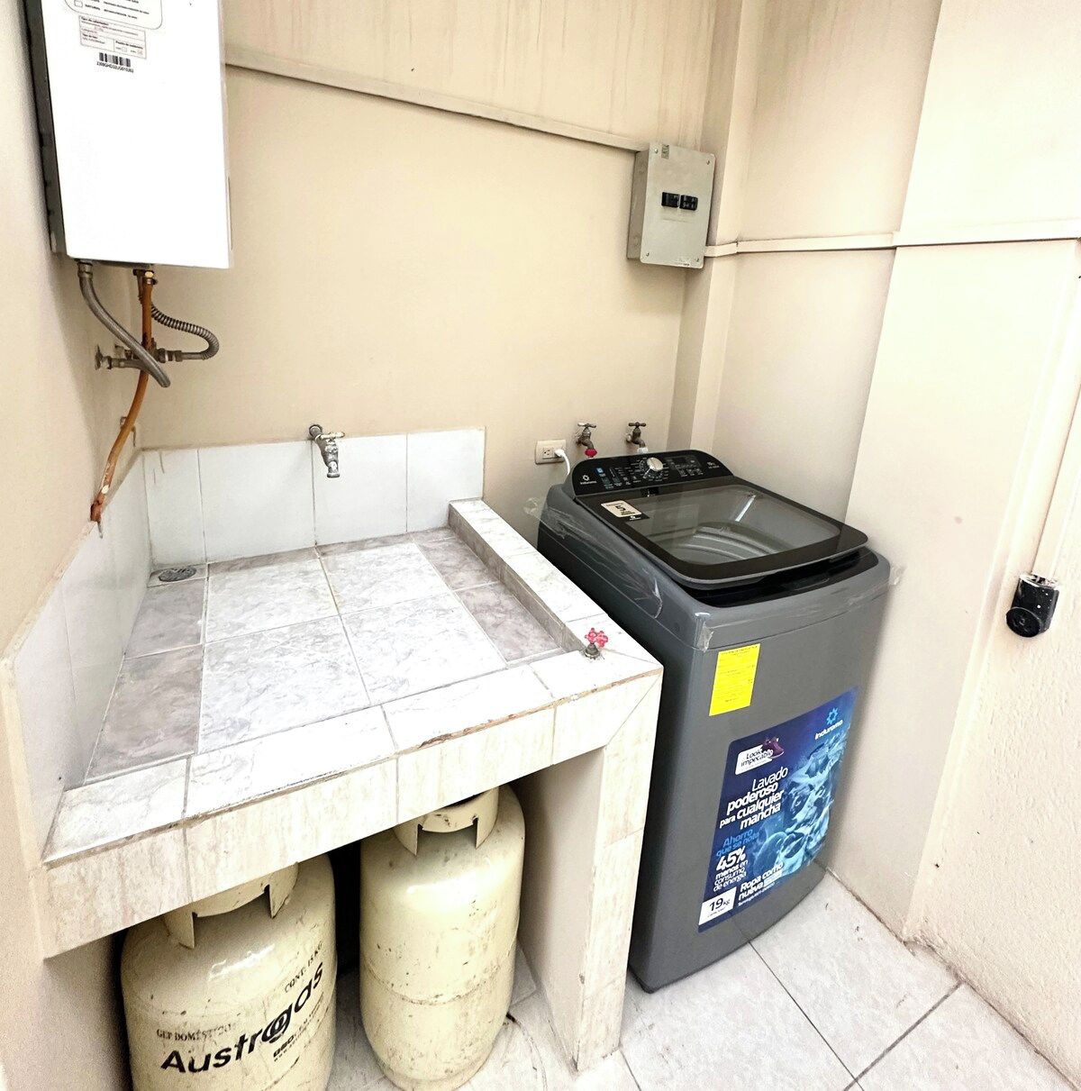Un petit espace dédié à la buanderie, comprenant un lave-linge, deux bouteilles de gaz et un chauffe-eau.