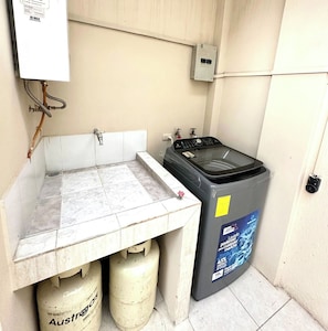 Un pequeño espacio para lavandería con lavadora, dos cilindros de gas y un calentador de agua.