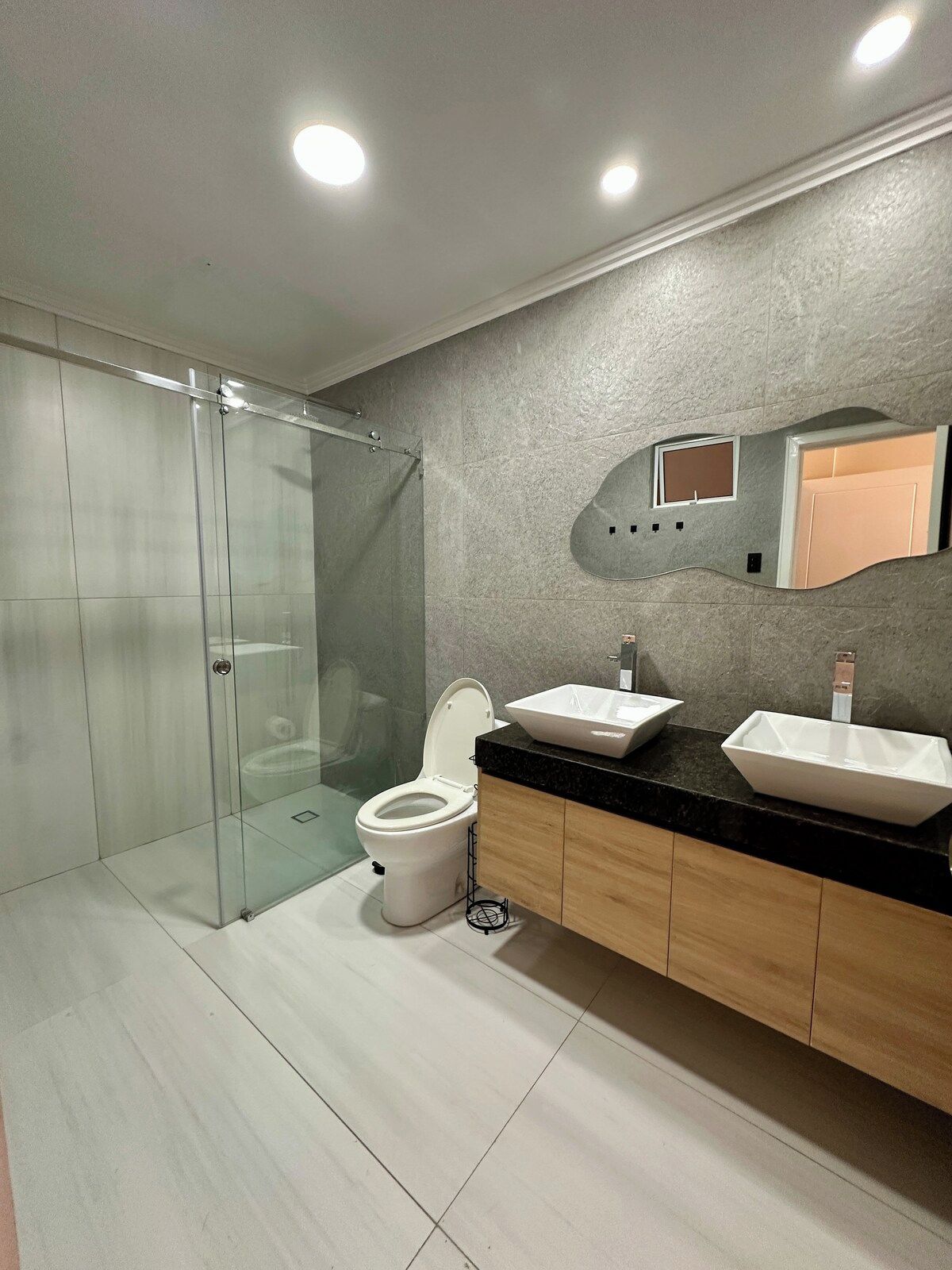Un baño moderno con cabina de ducha de vidrio, inodoro y tocador con dos lavamanos.
