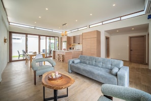 Un grand espace de vie comprenant un canapé, des fauteuils, une table basse en bois et une cuisine en arrière-plan.