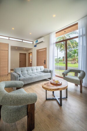 A modern living room with a grey sofa, two armchairs, a coffee table, and large windows with a view of palm trees.