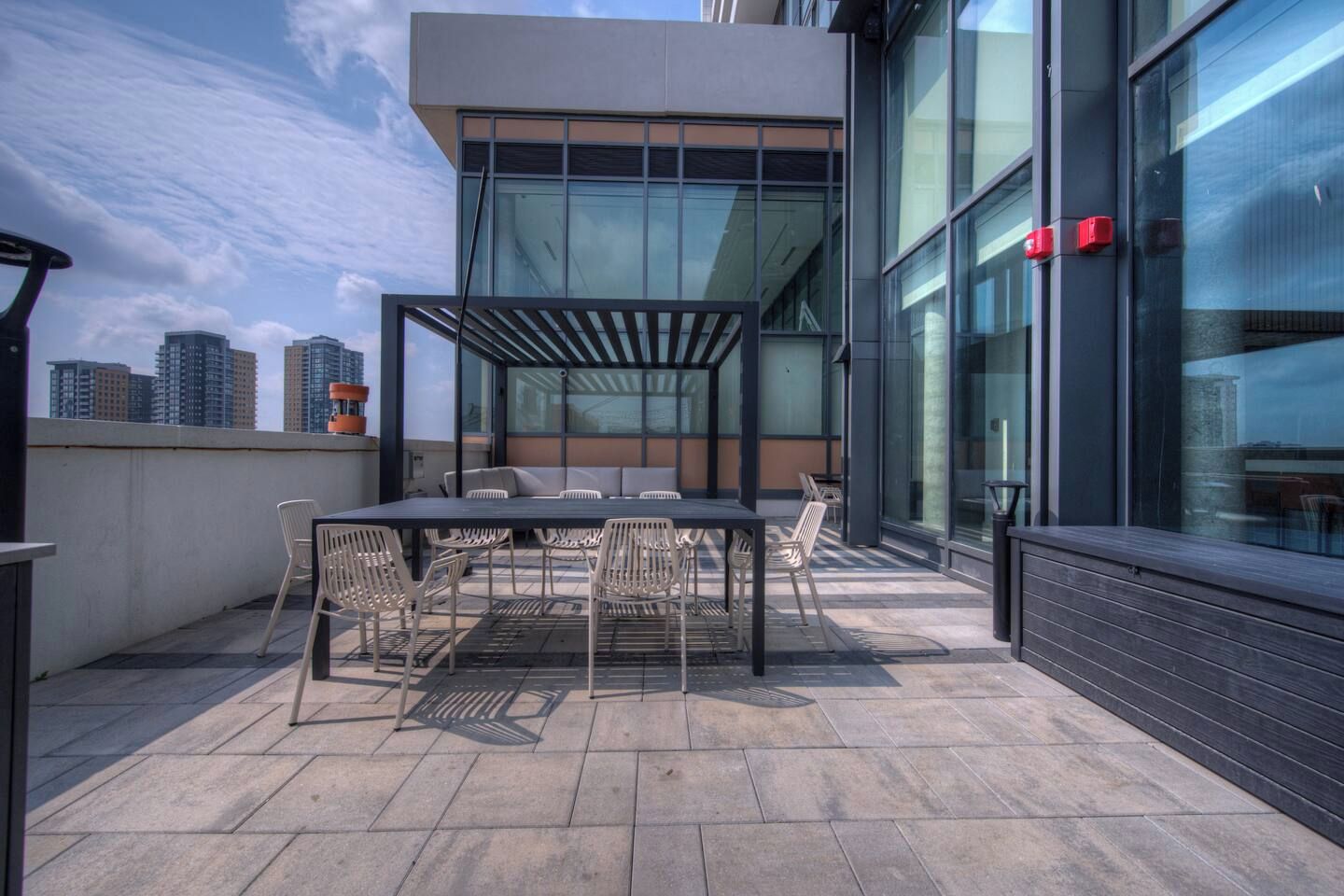 Een terras buiten met een tafel, stoelen, een pergola en uitzicht over de stad.