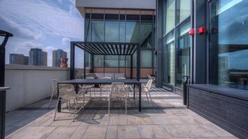 Een terras buiten met een tafel, stoelen, een pergola en uitzicht over de stad.