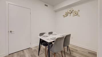 A dining area with a white table set for four, grey chairs, and a decorative wall piece.