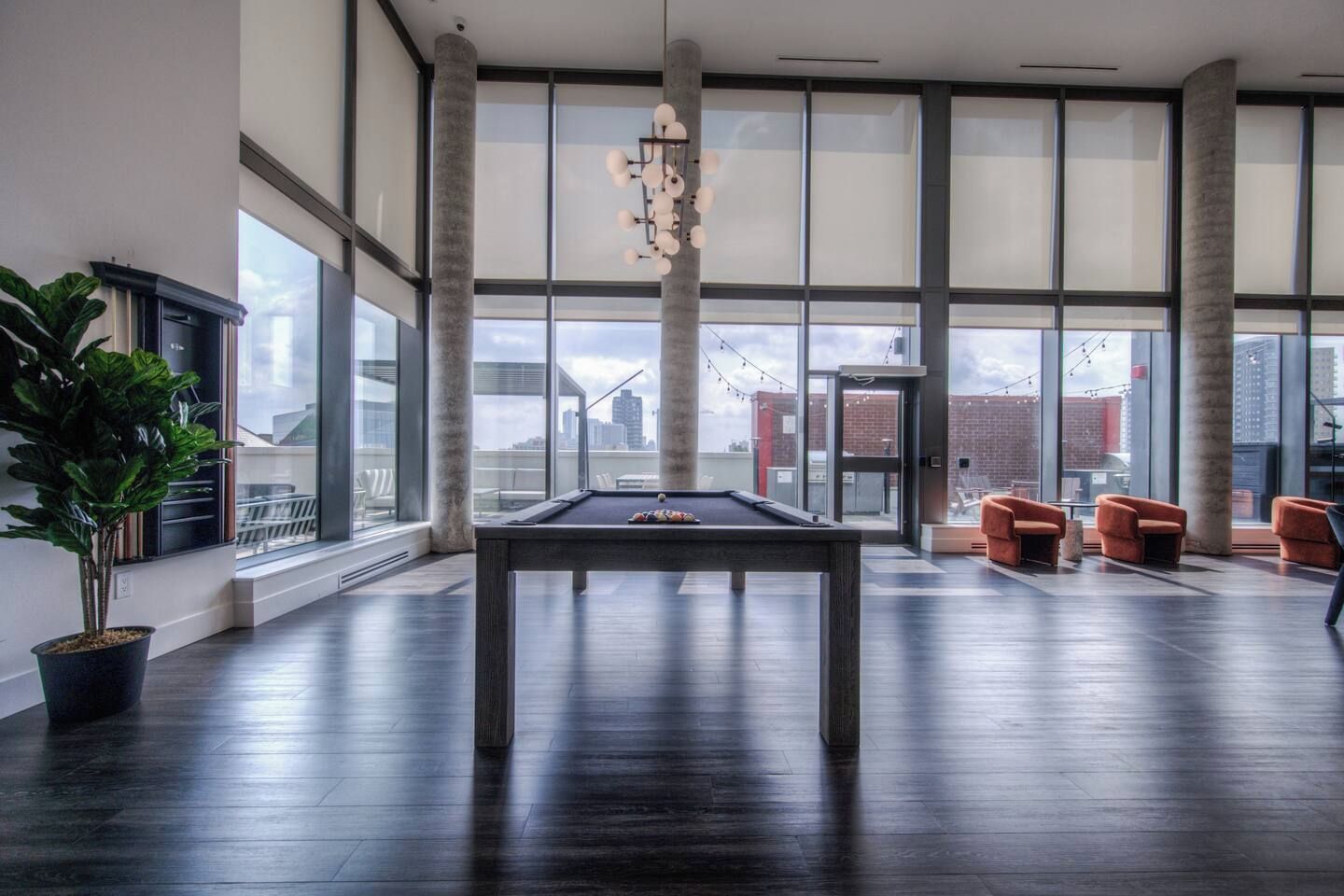 A spacious indoor area with a pool table, seating, and large windows offering views of the city.