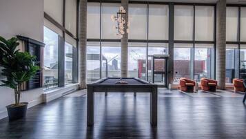 A spacious indoor area with a pool table, seating, and large windows offering views of the city.