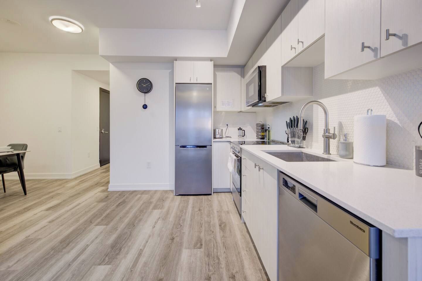 Una cocina moderna con armarios blancos, un refrigerador de acero inoxidable, un lavavajillas y un lavamanos con grifo.