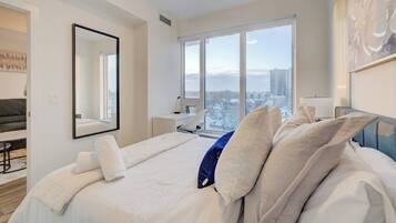A modern hotel room with a large bed, a desk, a chair, and a view of the city.
