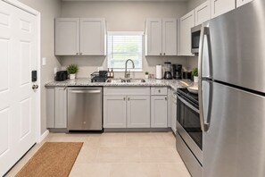 A modern kitchen with stainless steel appliances, grey cabinets, and a window providing natural light.