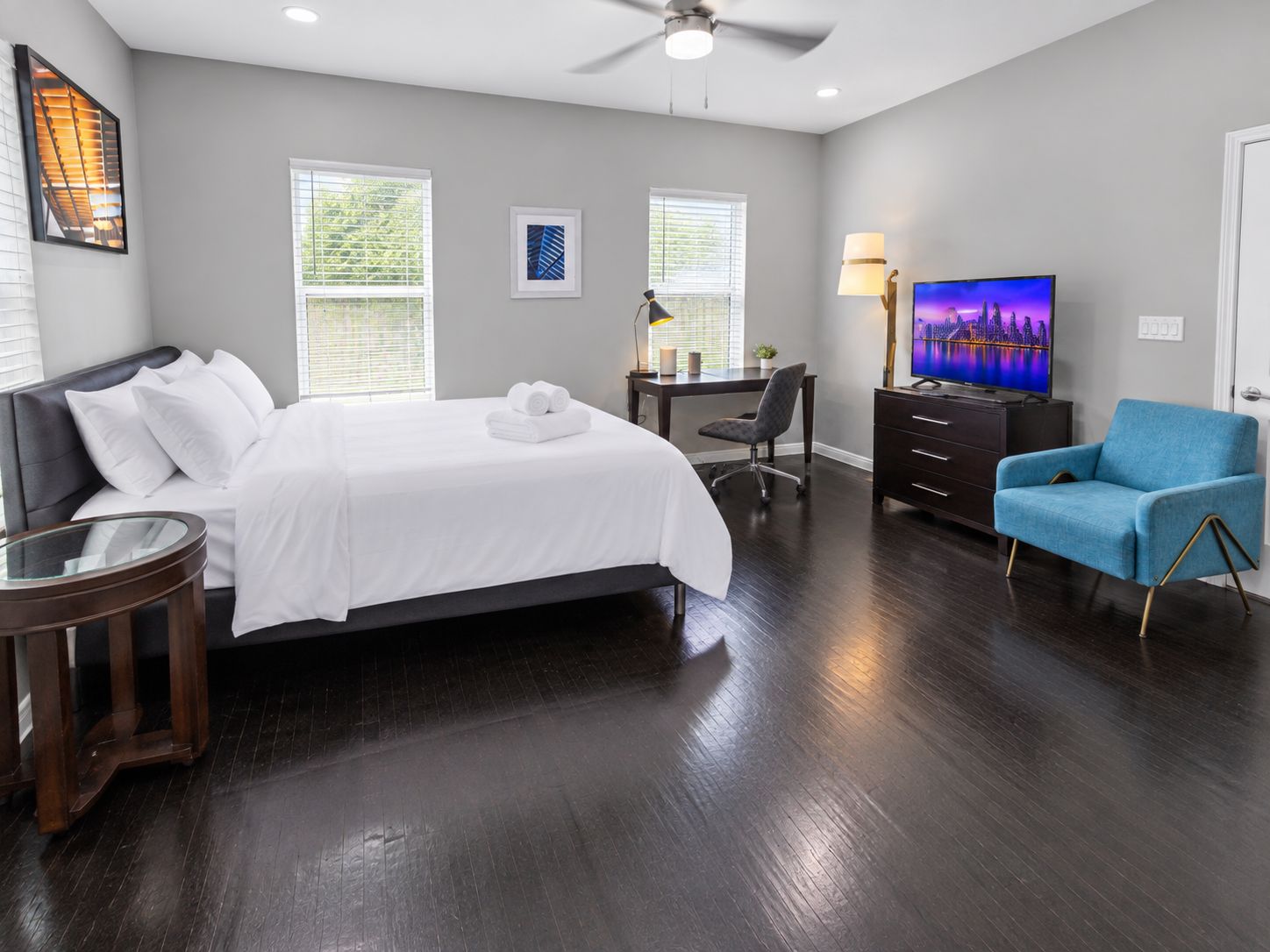 A hotel room with a bed, desk, chair, TV, and a blue armchair.