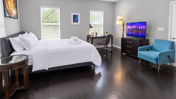 A hotel room with a bed, desk, chair, TV, and a blue armchair.