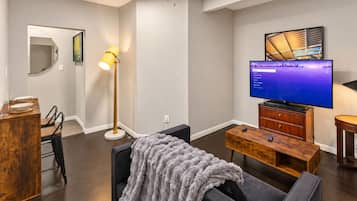 Una sala moderna con una televisión de pantalla plana, una mesa de centro de madera, un sofá y una lámpara de pie.