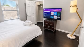 A hotel room with a bed, a flat-screen TV mounted on the wall, a wooden dresser, and a floor lamp.