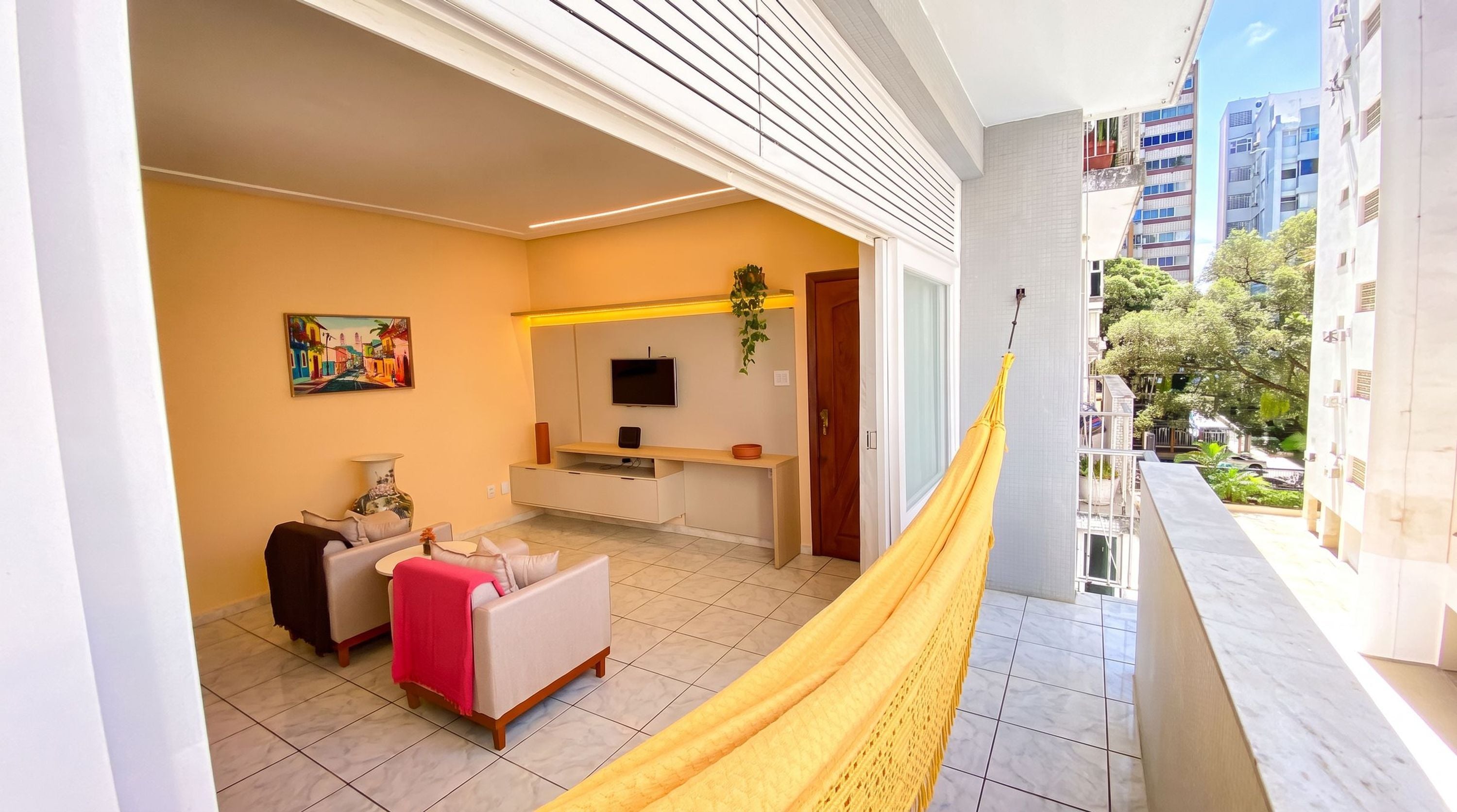 Un balcon avec un hamac jaune, un canapé, une télévision et un tableau accroché au mur.