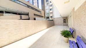 A modern outdoor corridor with tiled flooring, a potted plant, and a bench. - Apto c Varanda e Vaga pr x a Praia Porto da Barra (Salvador)
