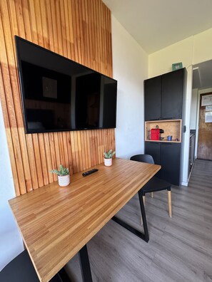 A modern room with a wooden panel wall, a flat-screen TV, a wooden table, two potted plants, and a small kitchenette area. - Vista al lago a pasos del Centro Cívico (San Carlos de Bariloche)