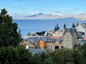 A coastal town with traditional buildings, a prominent clock tower, and a view of the sea and mountains in the background. - Vista al lago a pasos del Centro Cívico (San Carlos de Bariloche)