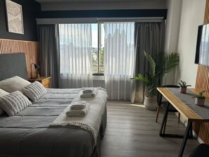 Ein modernes Hotelzimmer mit einem Bett, einem Schreibtisch, einer Zimmerpflanze und Blick aus dem Fenster.