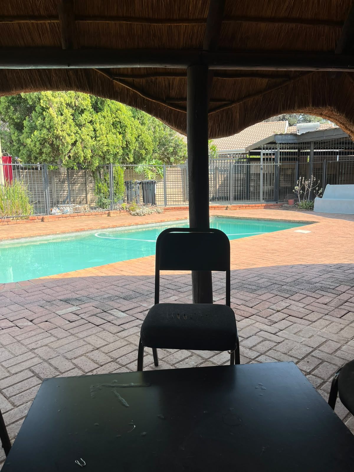 A covered outdoor area with a pool, a chair, and a table.