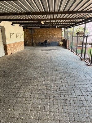 An open covered area with a brick wall and a metal roof, featuring a grill and seating area.