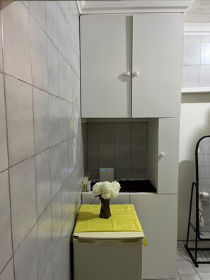 Una cocina con un armario blanco, un tapete amarillo sobre la encimera y un florero blanco.