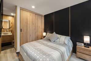 Ein Schlafzimmer mit einem Bett, Nachttischlampen, einem Nachttisch, einer Kommode, einem Spiegel und einem Holzschrank.
