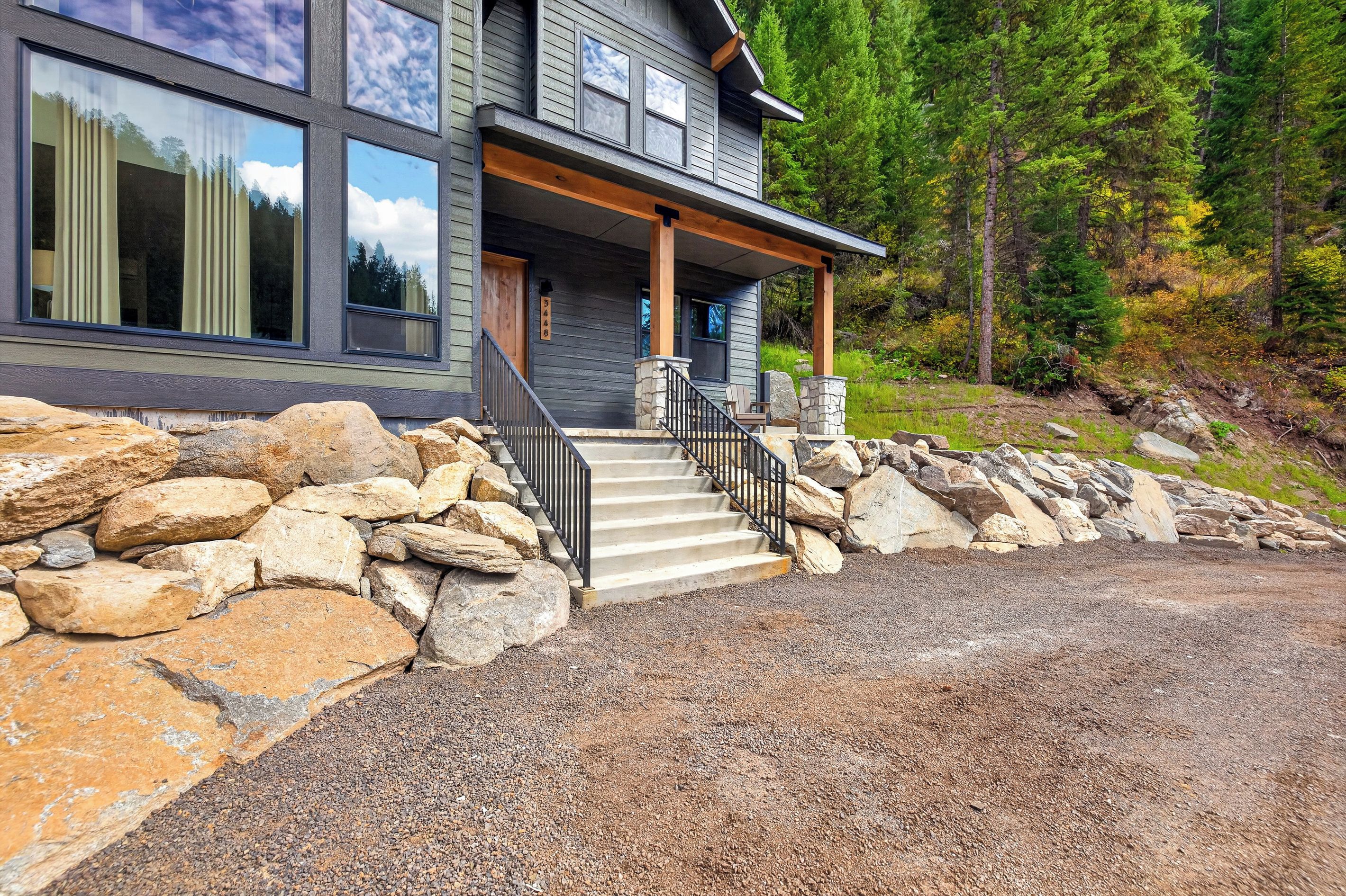 A modern two-story house with a stone foundation, a wooden porch, and a stone staircase leading to the entrance.