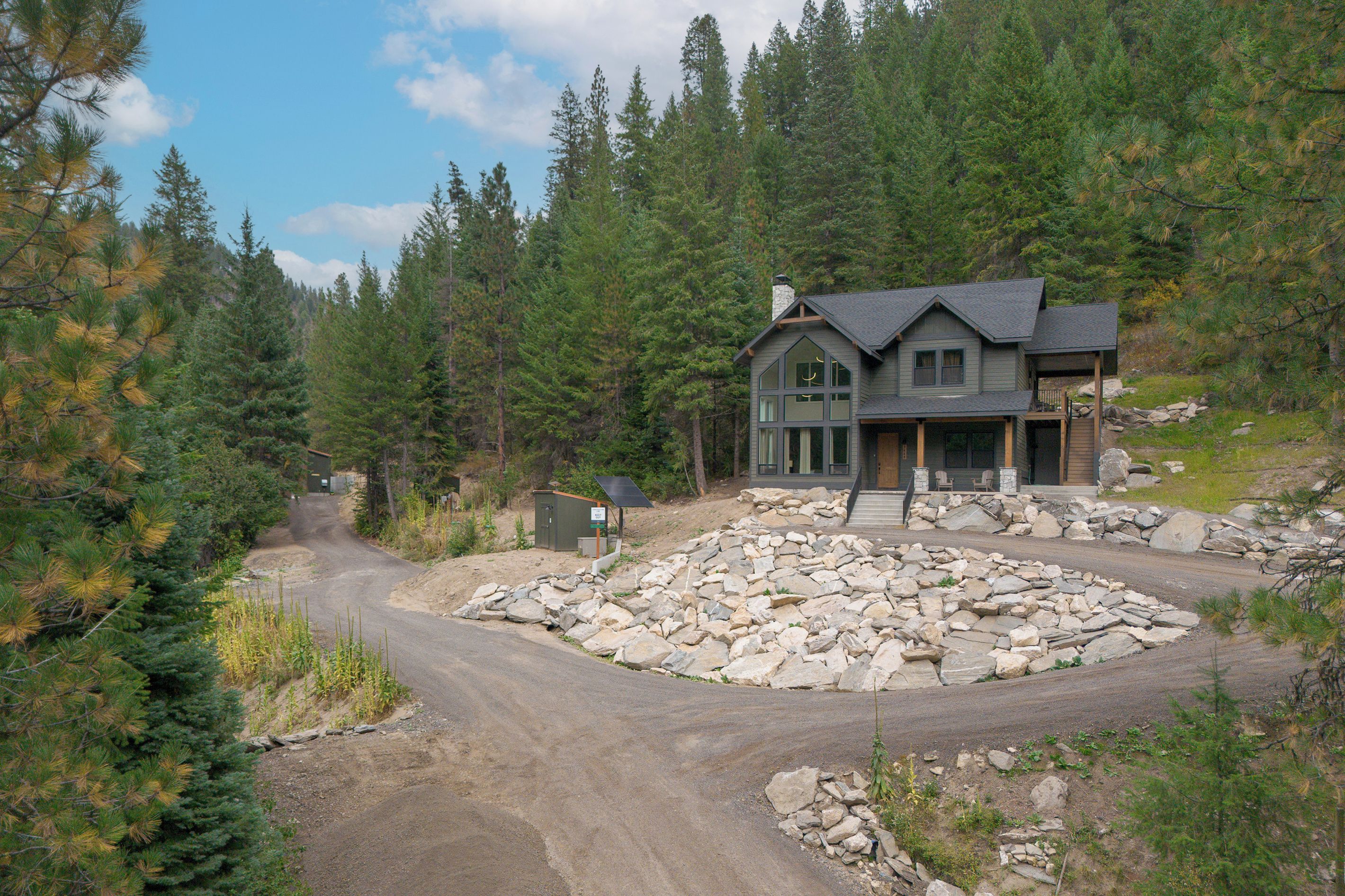 Una casa de dos pisos con base de piedra, rodeada por un paisaje natural con pinos.