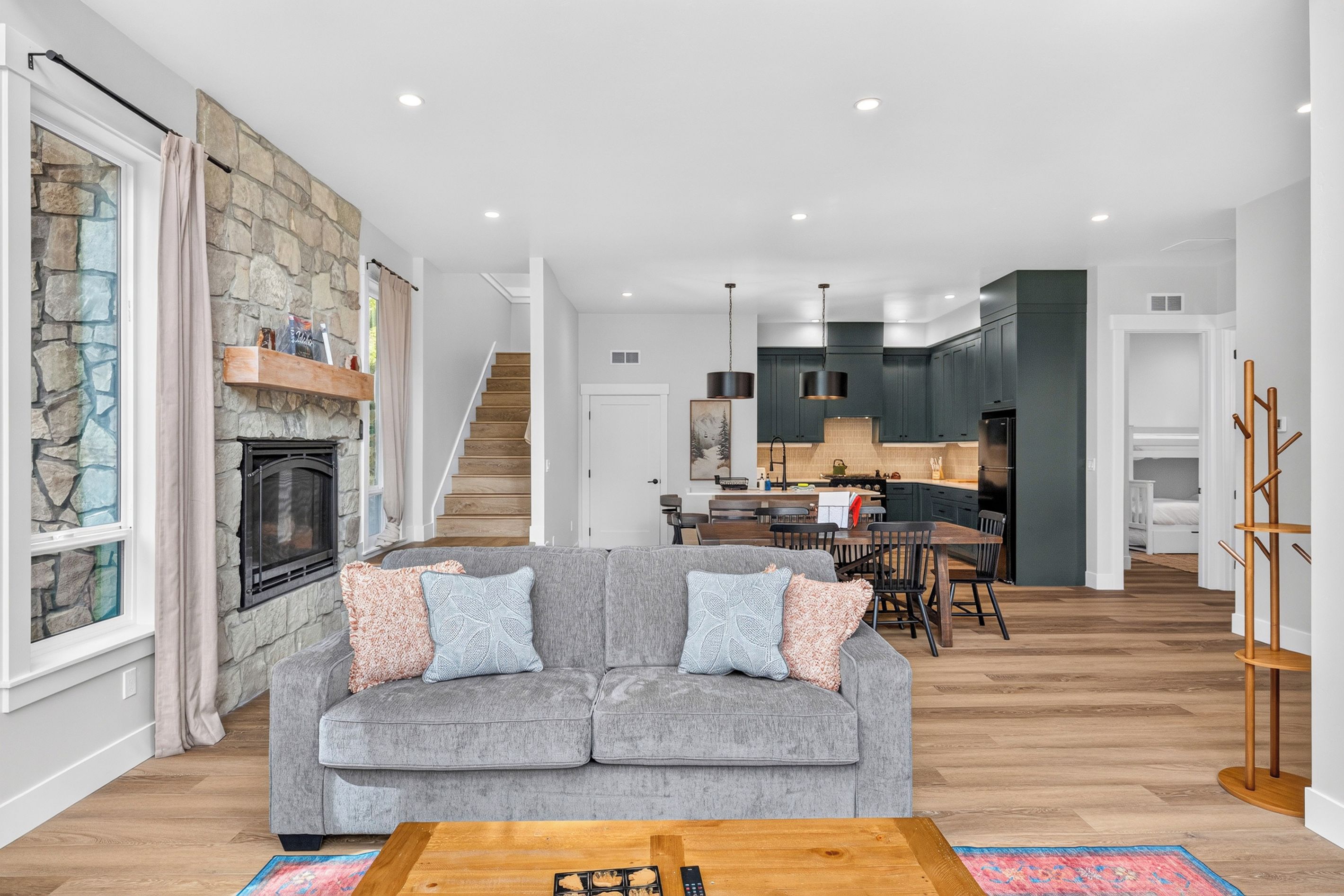 A modern living room with a grey sofa, a fireplace, a dining area, and a kitchen.