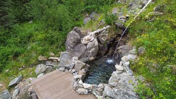 A wooden deck overlooking a natural hot spring with a stone wall and rocks.