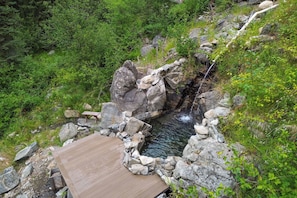 A wooden deck overlooking a natural hot spring with a stone wall and rocks. - Private Hot Spring | Views | River | Brundage (New Meadows)